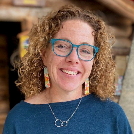 Jen wears blue glasses and colorful shirt and smiles for headshot